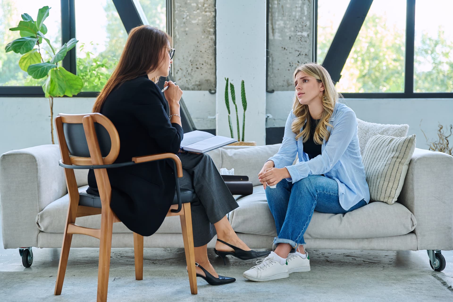 A young woman talking with a psychologist seated across from her in a light-filled therapy space