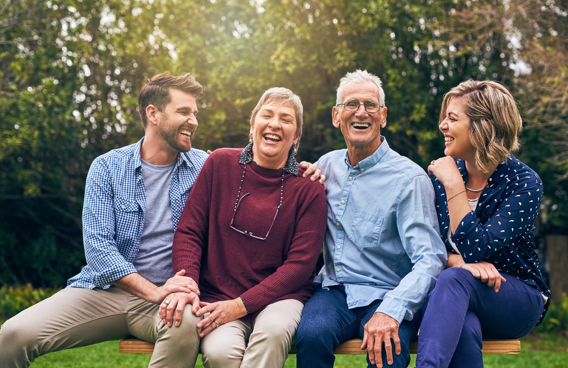 Two generations of a family laughing together on a park bench surrounded by trees
