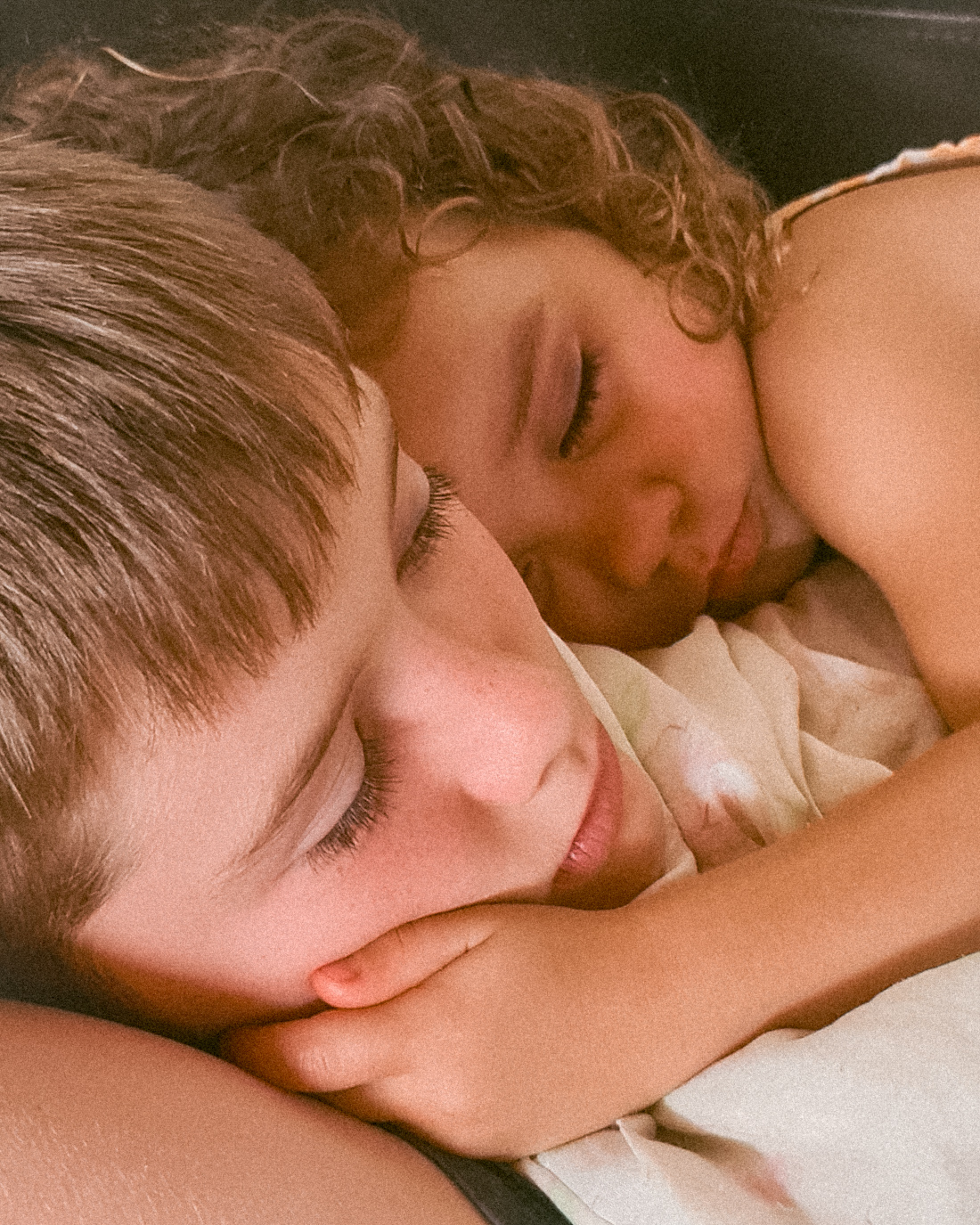 Two young siblings resting closely together, smiling with their eyes closed