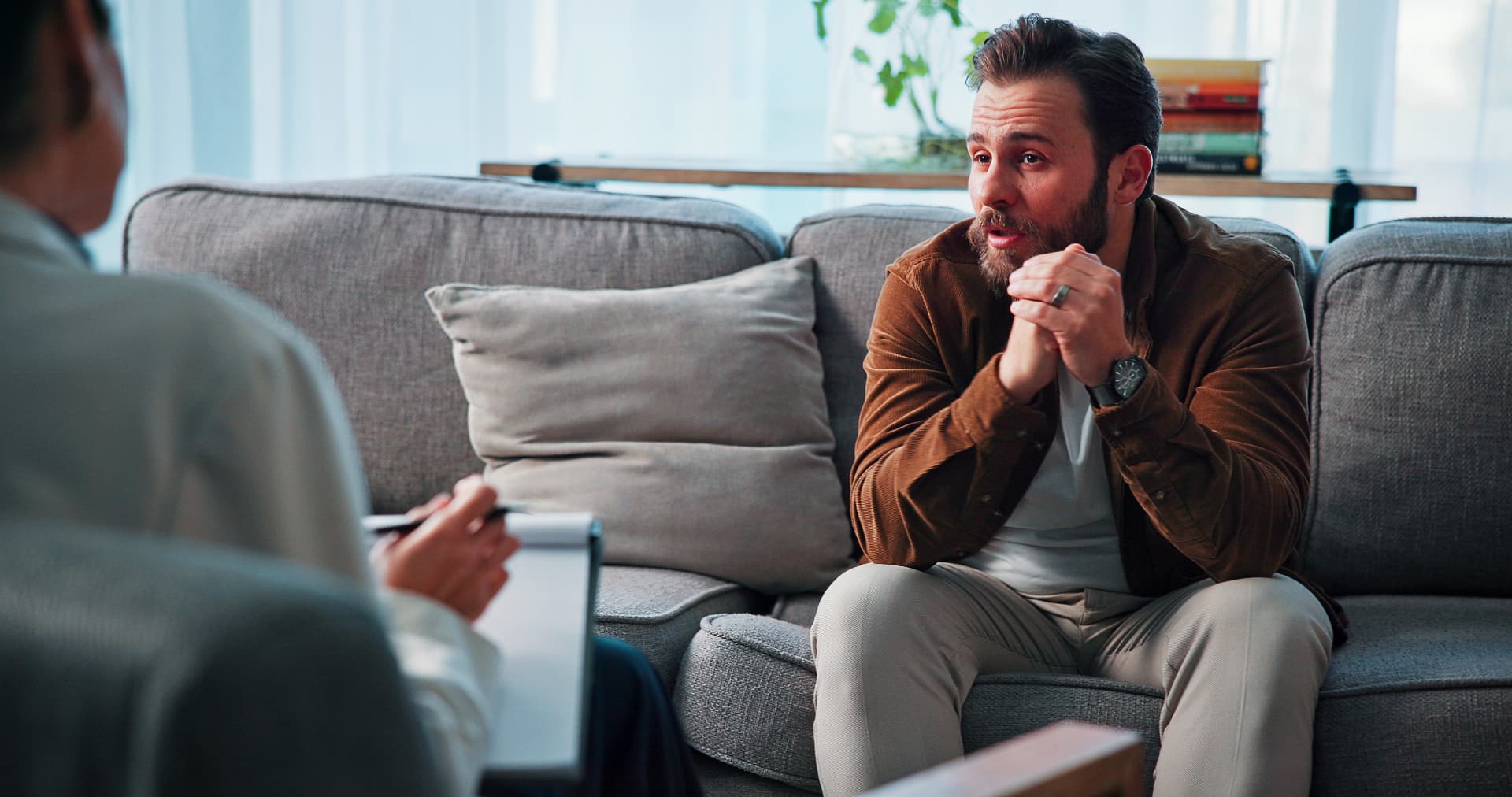 A man speaking openly with a clinician taking notes in a bright consulting room